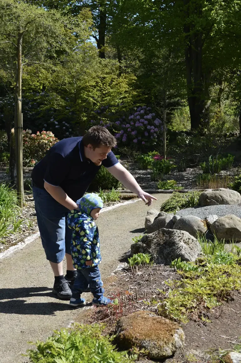 Mand peger og viser sit barn en blomst i haven